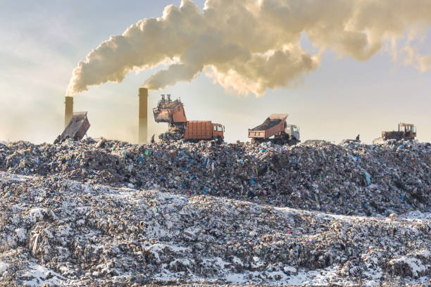 Waste management Image Dump trucks unloading garbage over vast landfill. Smoking industrial stacks on background. Environmental pollution. Outdated method of waste disposal. Survival of times past.